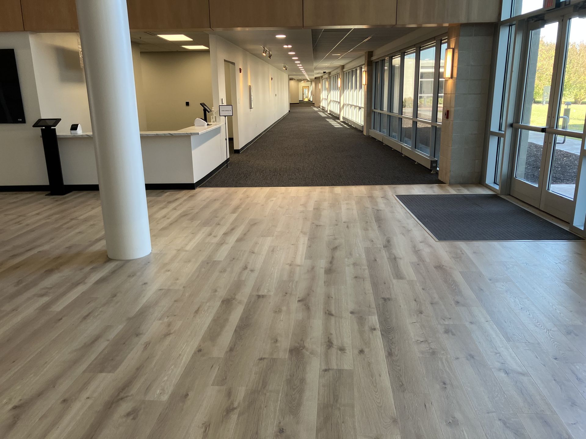 Hallway with wood-look floor, carpeted area, and windows. White columns, reception desk, and entryway.