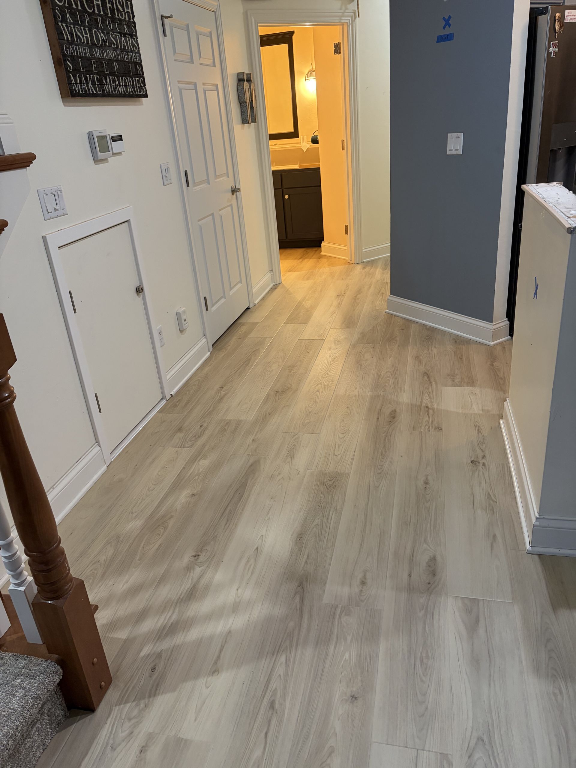Hallway with light wood-look flooring, white walls, and a door leading to a bathroom.