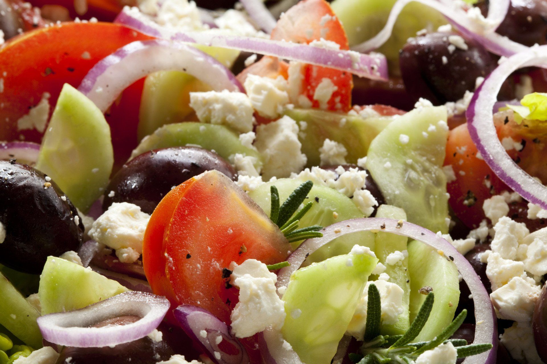 A close up of a salad with tomatoes , cucumbers , onions , olives and feta cheese.