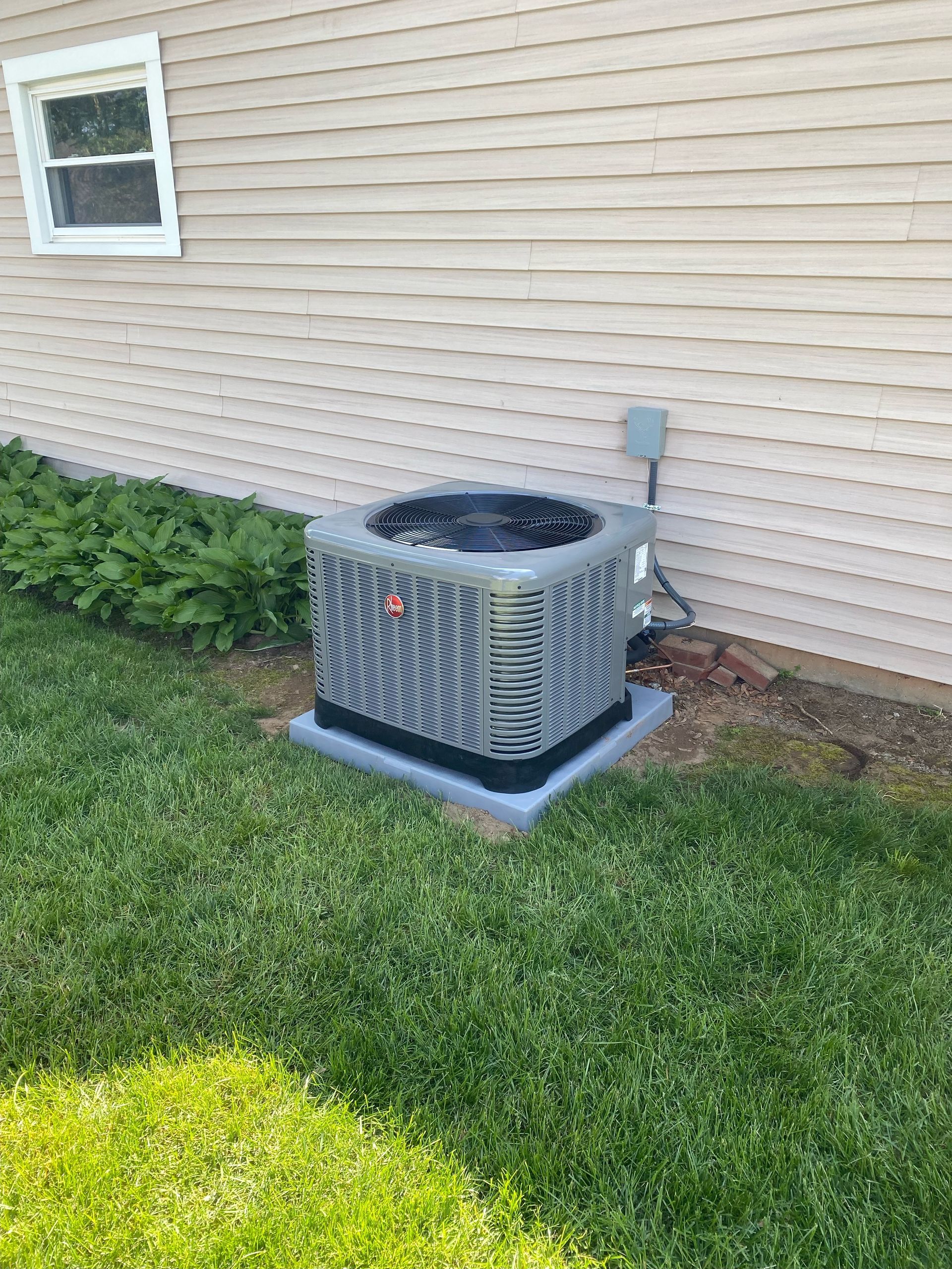 An air conditioner is sitting in the grass next to a house.