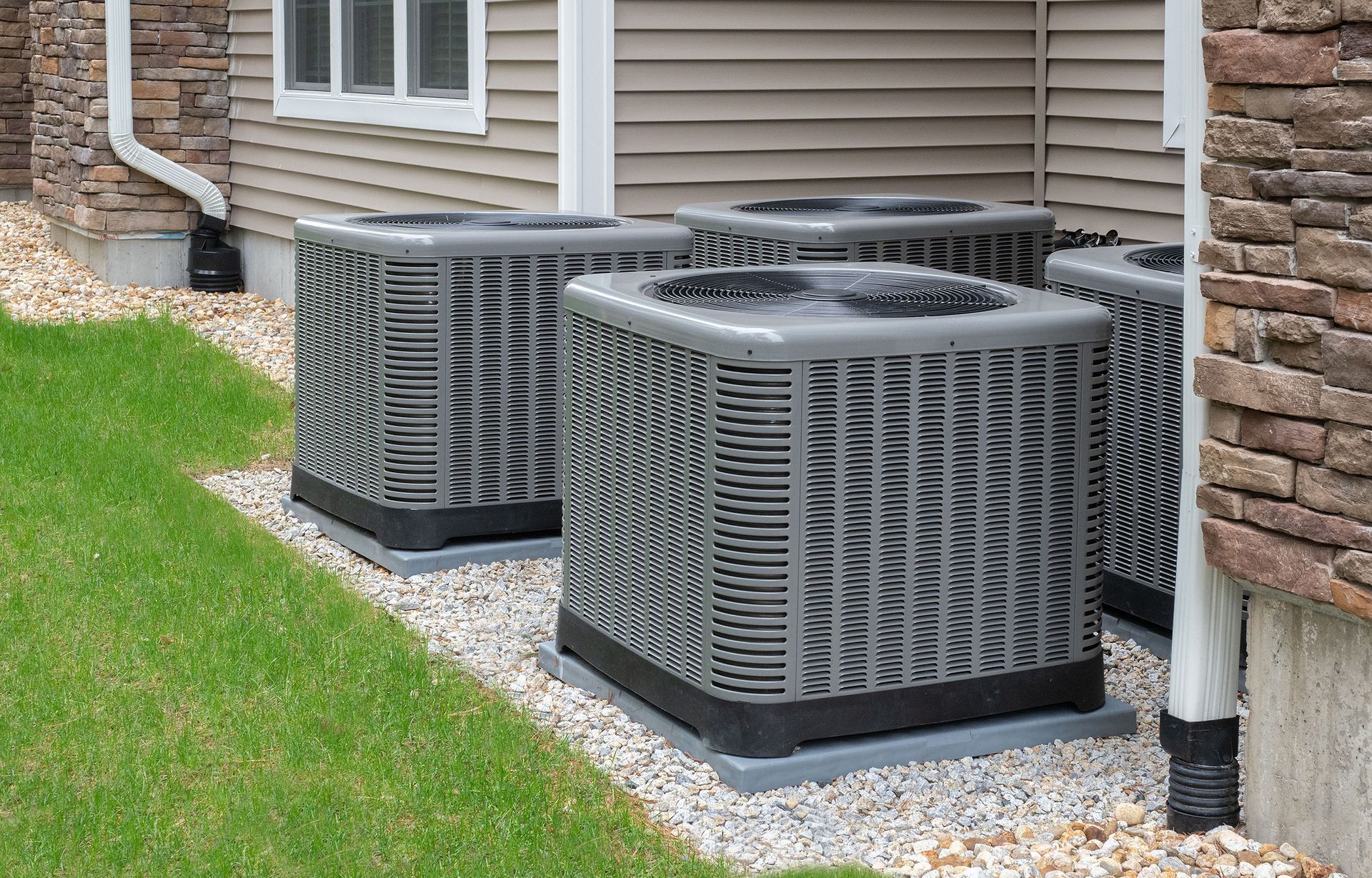 Three air conditioners are sitting on the side of a house.