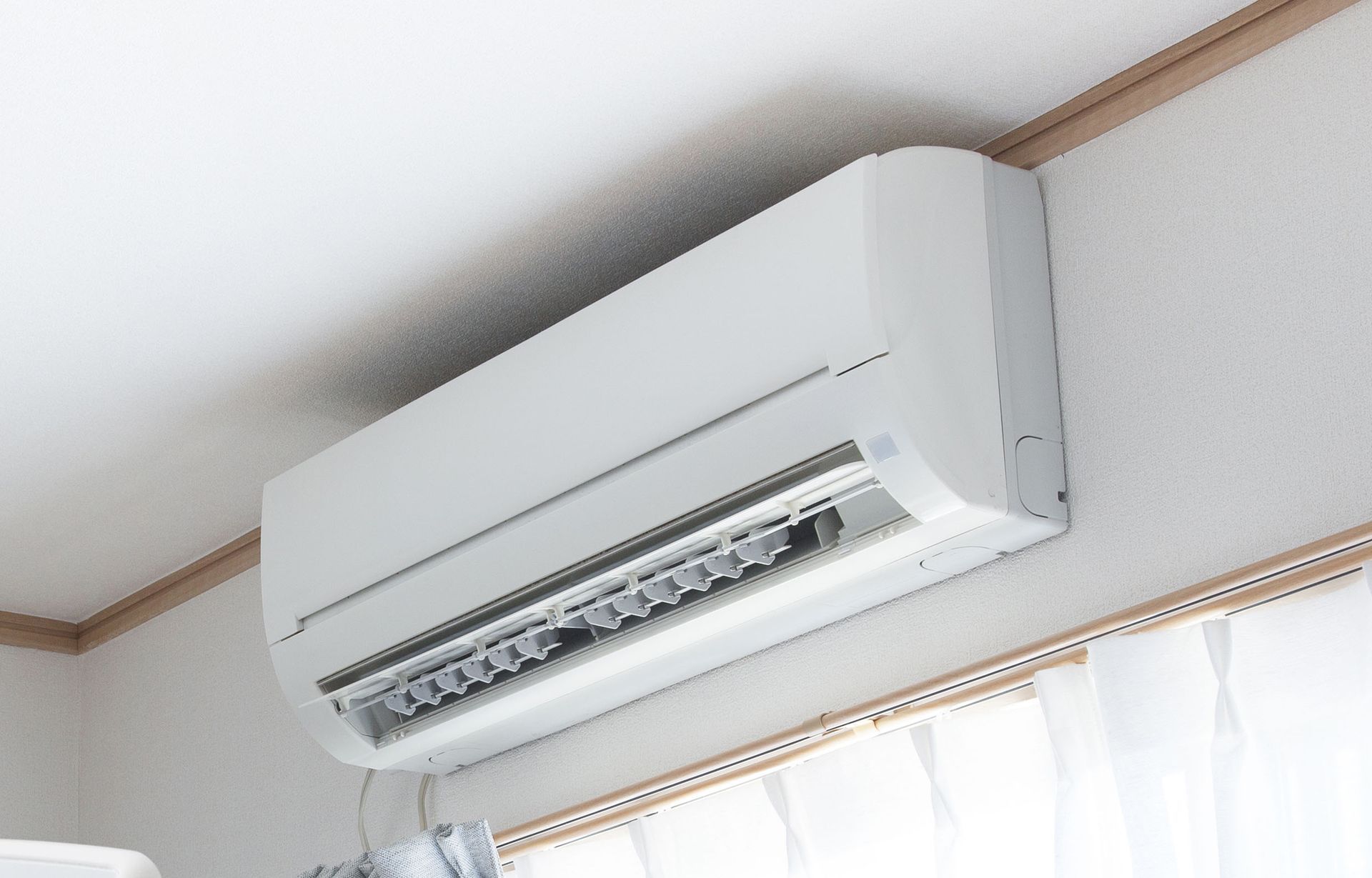 A white air conditioner is hanging from the ceiling in a room next to a window.