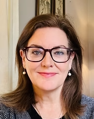 A woman wearing glasses and earrings is smiling for the camera.