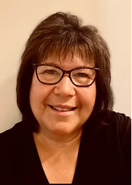 A woman wearing glasses and a black shirt is smiling for the camera.