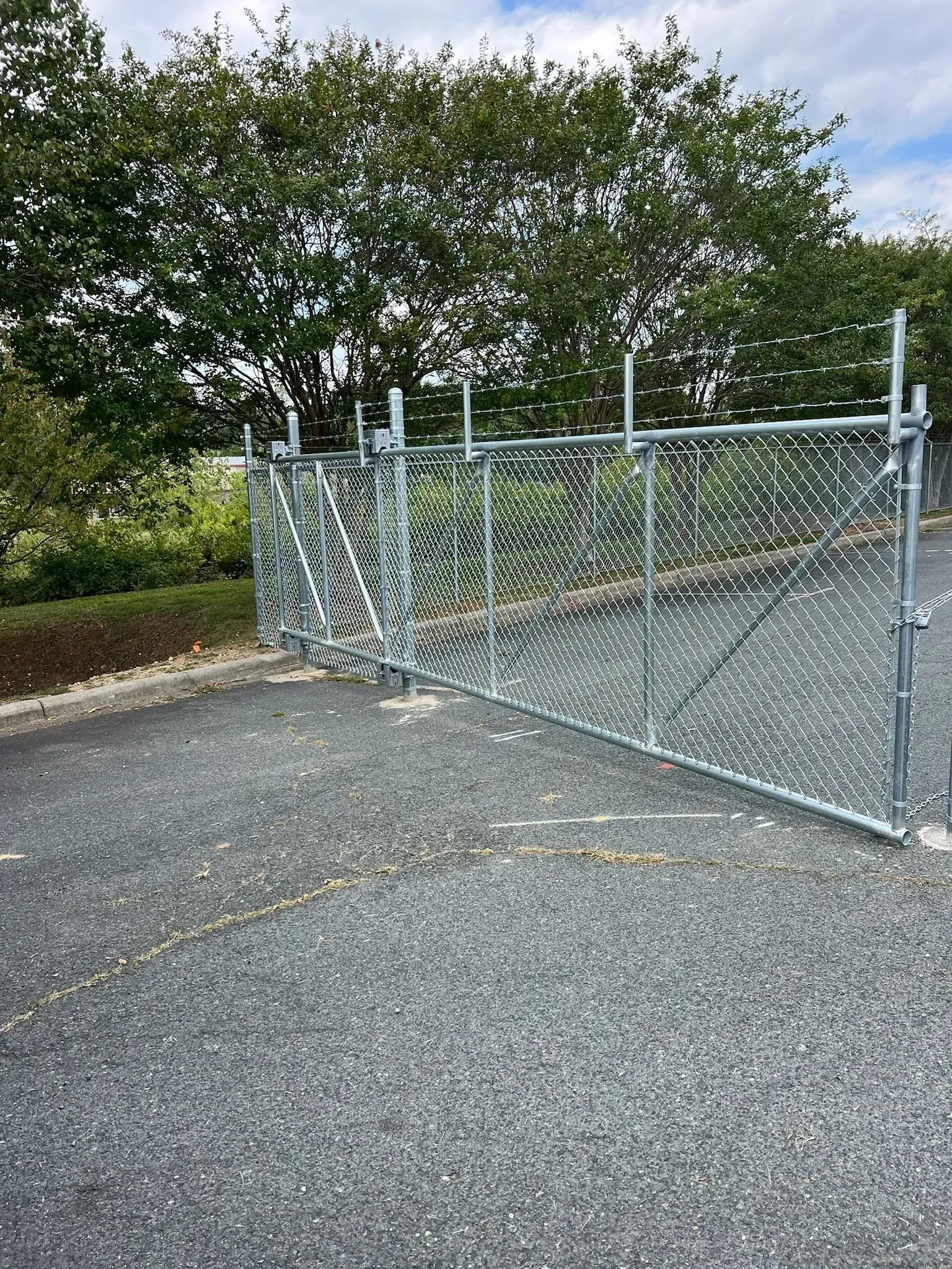 Chain link gate and fence on asphalt driveway, trees in background.