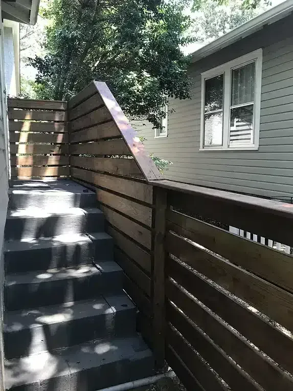 Outdoor concrete stairs with a wooden horizontal slat fence beside them, leading up to a building.