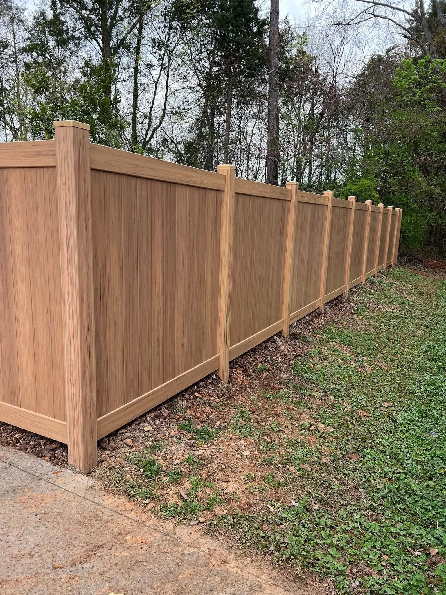 Brown vinyl privacy fence in a grassy area with trees in the background.