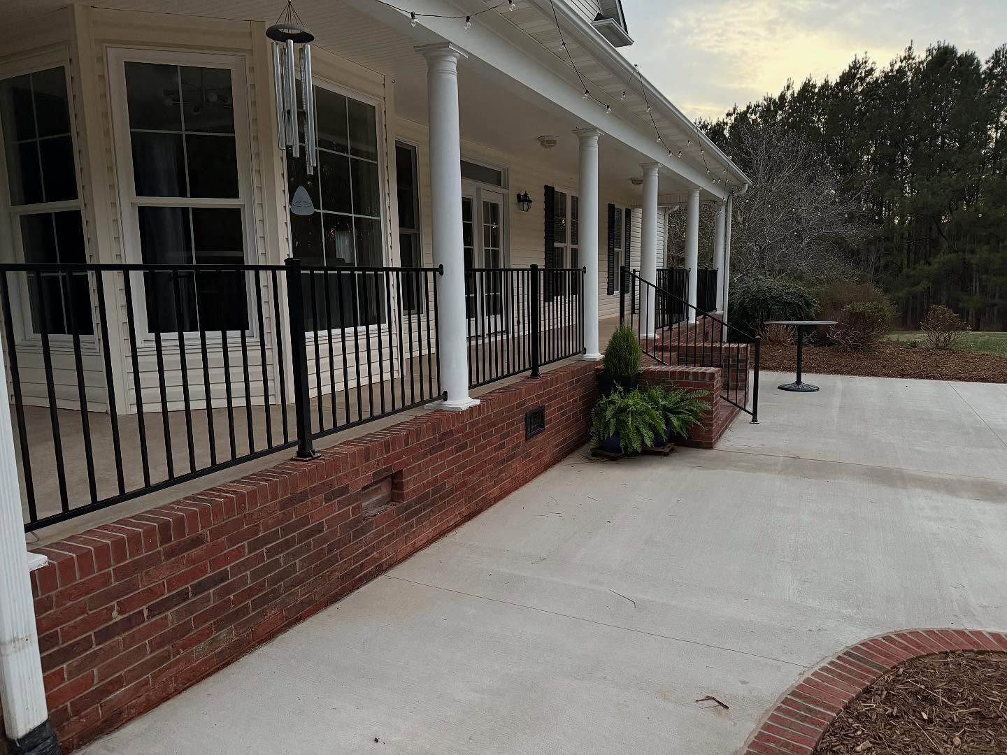 Covered porch with black railing, brick base, white columns, and concrete patio.
