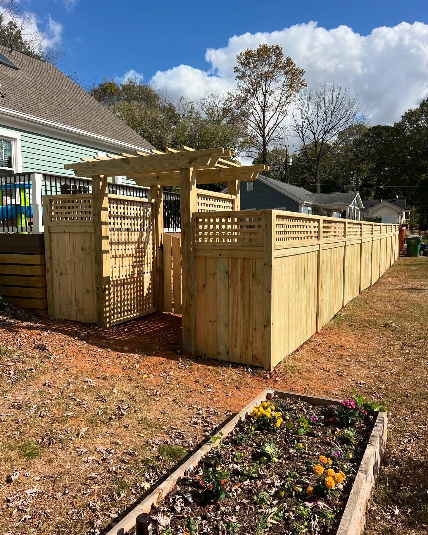 Wooden fence with gate and arbor leading into backyard with a garden box in the foreground.