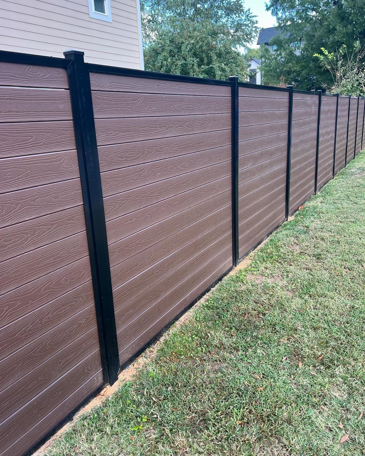 Brown horizontal-slatted privacy fence with black posts, bordering green grass.