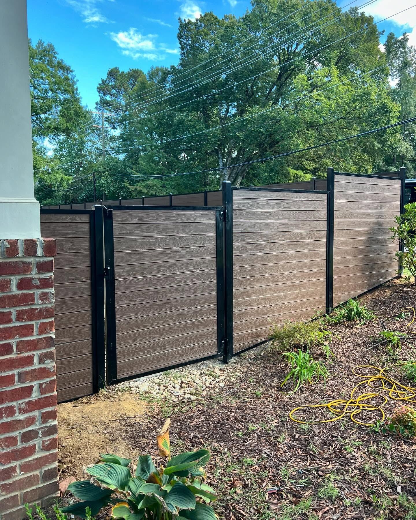 Brown and black privacy fence next to a brick building.