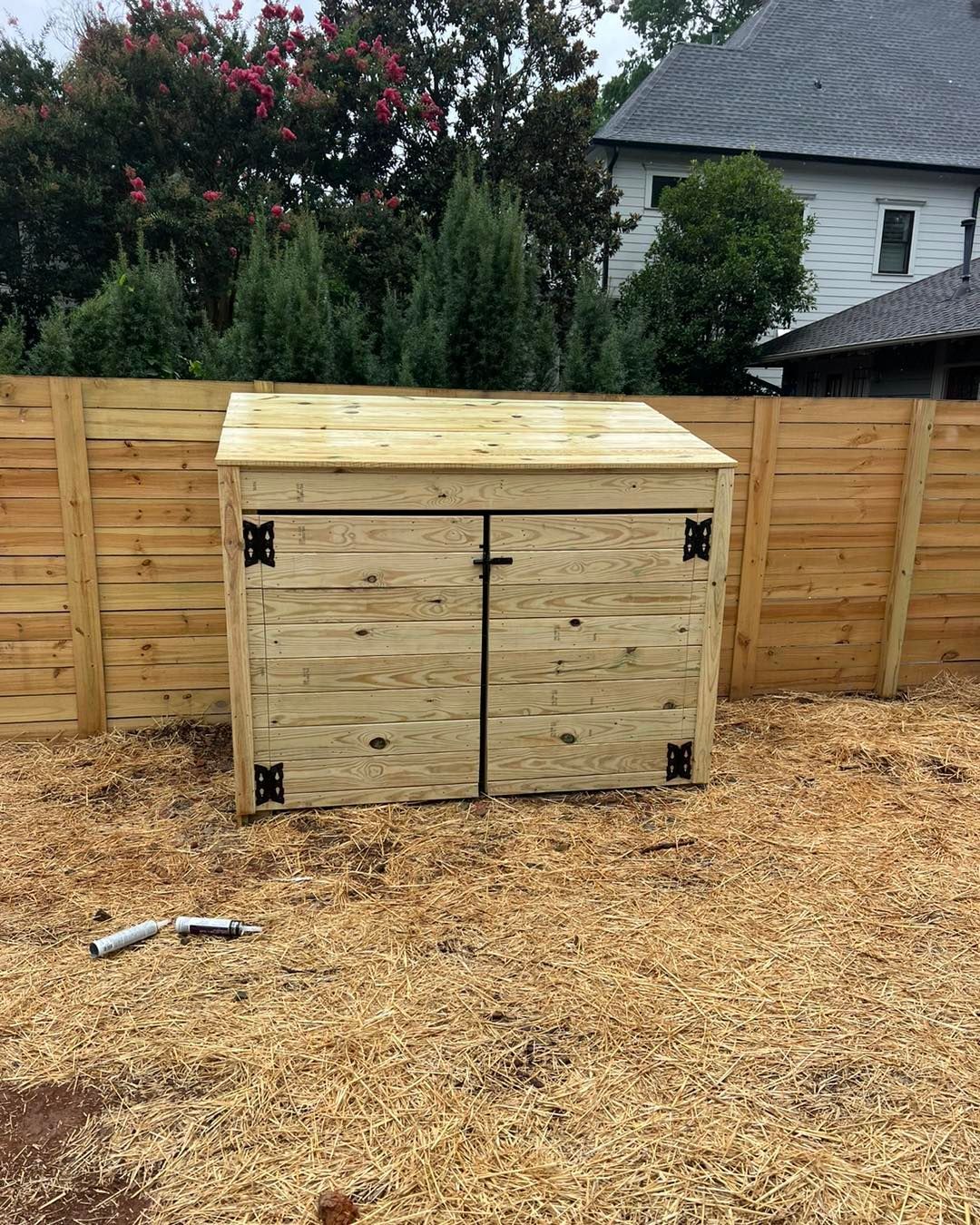 Wooden storage shed with a sloped roof in a backyard, beside a wooden fence.