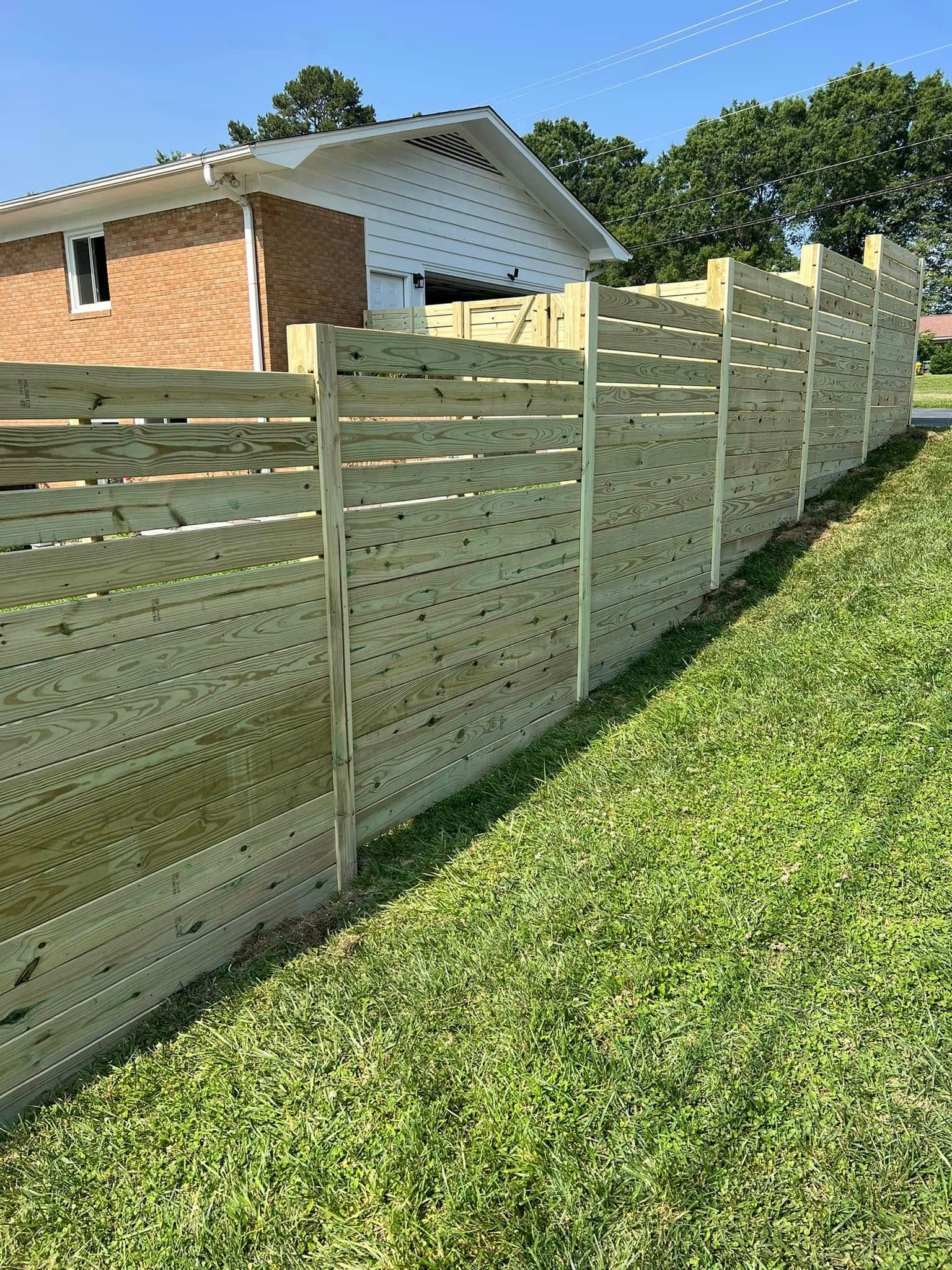 Wooden horizontal slat fence in front of a brick house and grass.