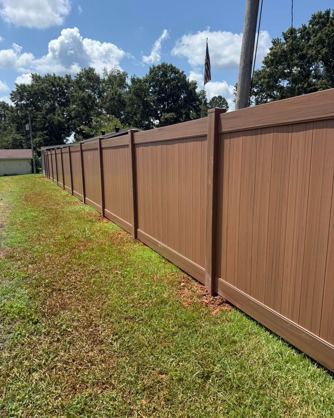 Brown privacy fence in a grassy yard under a blue sky with clouds.