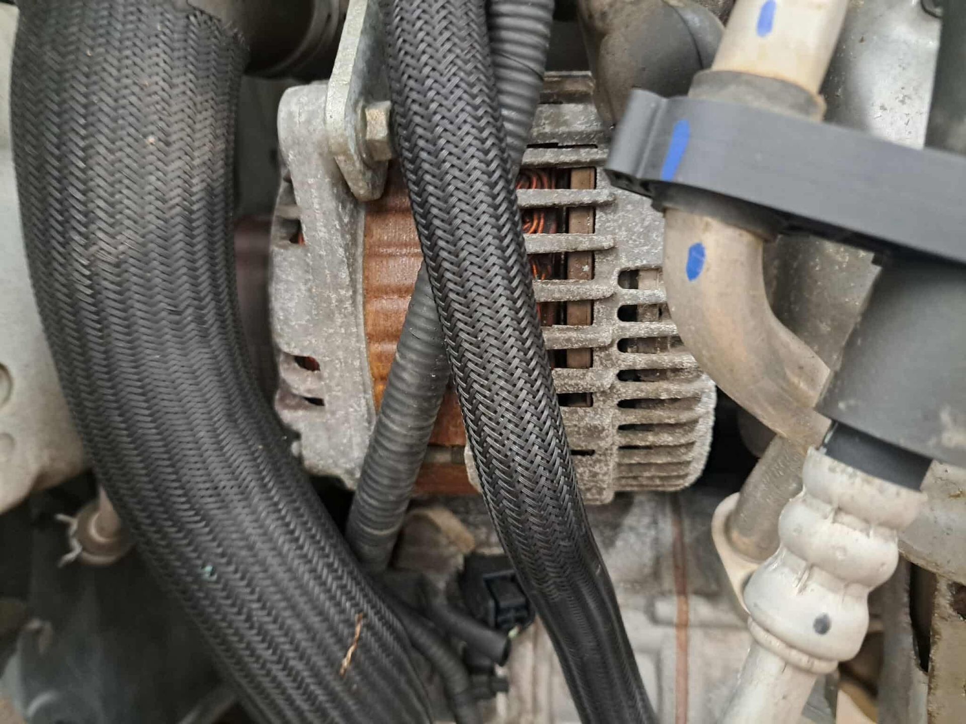 Close-up of a car engine showing a rusty alternator surrounded by black hoses and pipes.