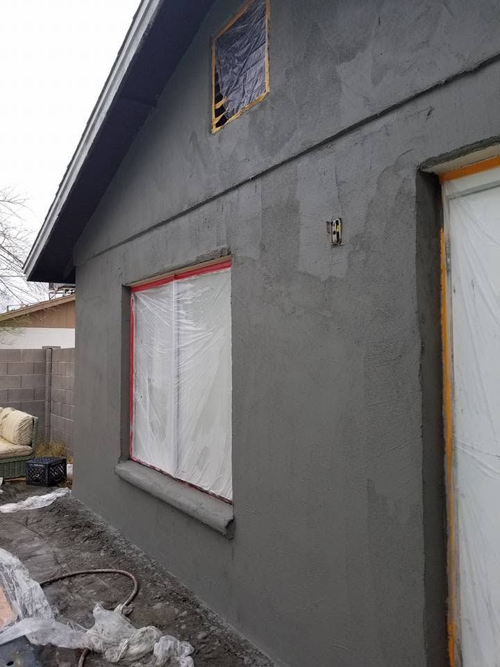 Gray stucco house exterior with covered windows and a white door under construction.