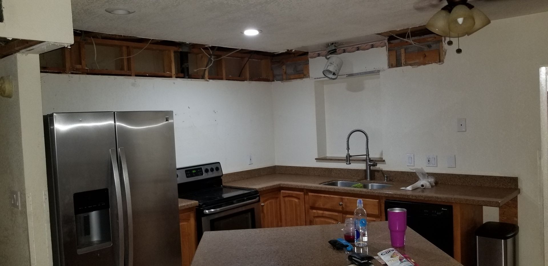 Renovated kitchen with stainless steel fridge, stove, wood cabinets, and a sink under bright ceiling lights