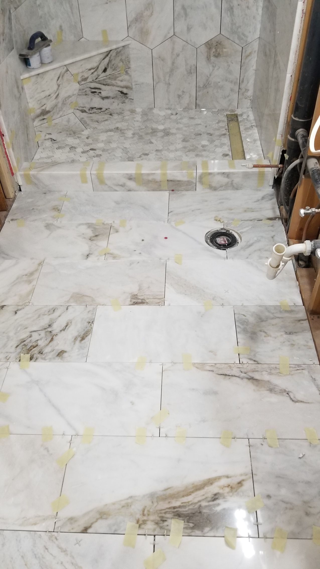 Marble-tiled bathroom floor with a shower curb and plumbing fixtures along the walls