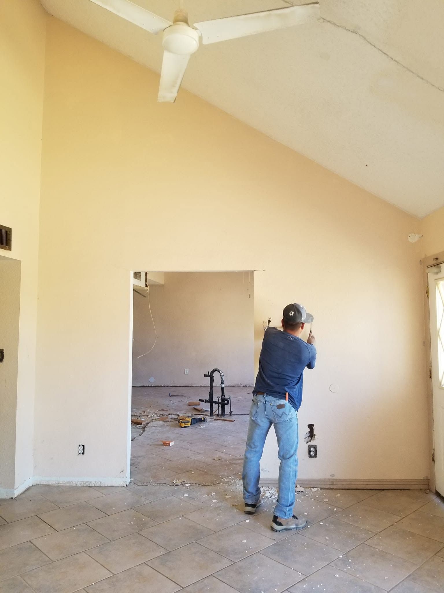 Person holding a tool in a beige room with a large wall opening and tiled floor.