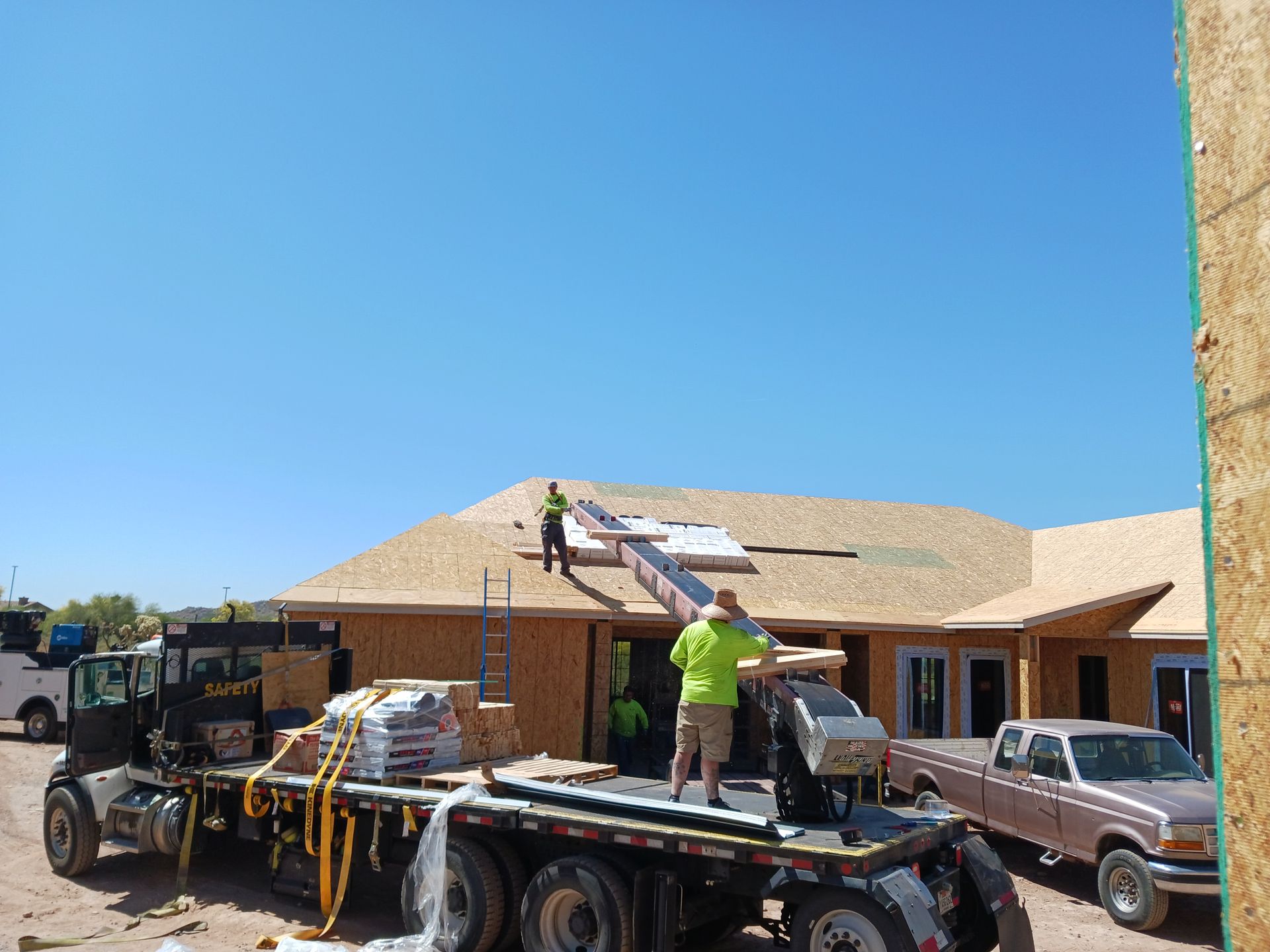 Workers load roofing materials onto a flatbed truck at a house under construction.