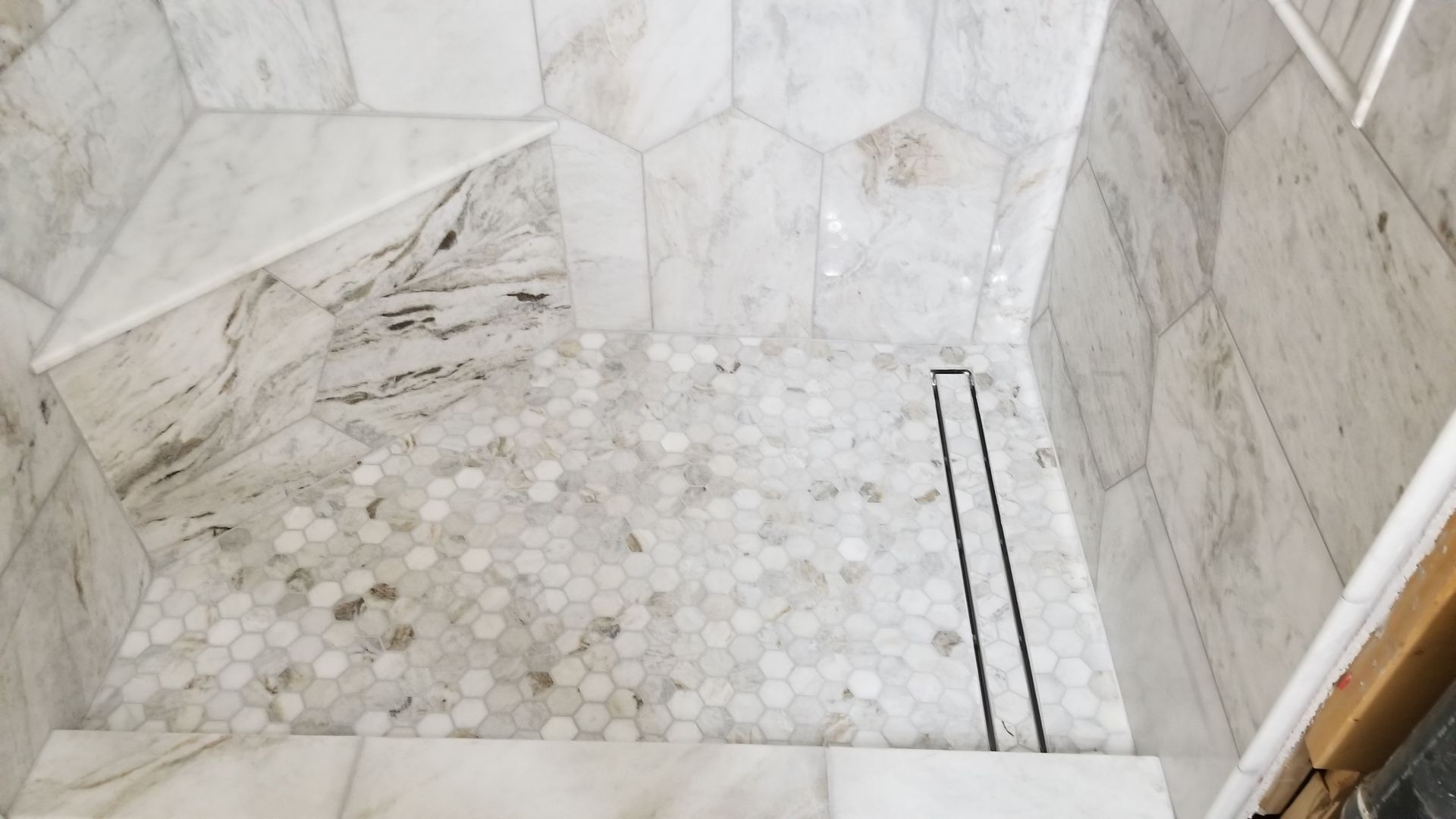 Marble-tiled shower with white walls, mosaic floor, and a linear drain