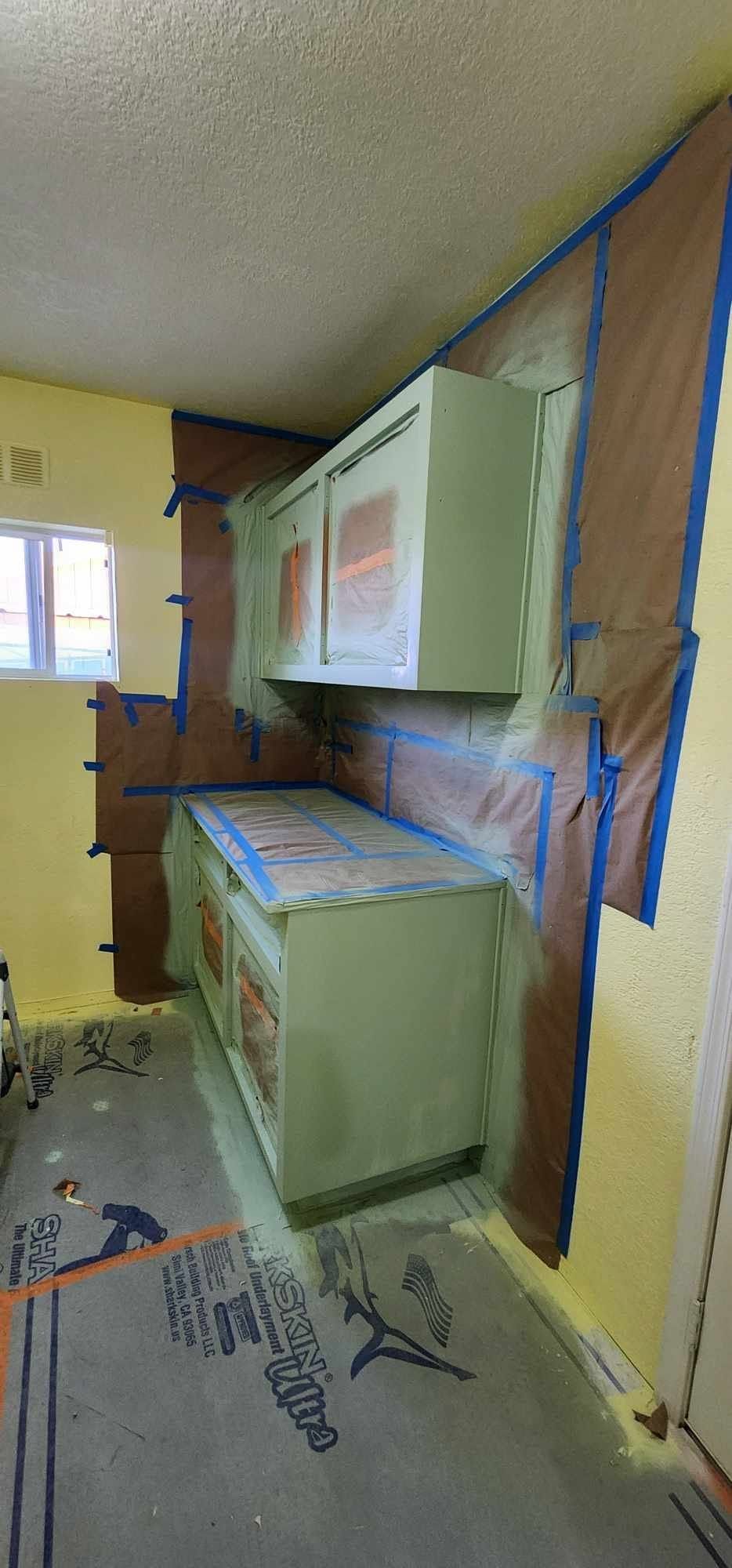 Partially finished kitchen with white cabinets, a countertop, and plastic-covered walls during renovation