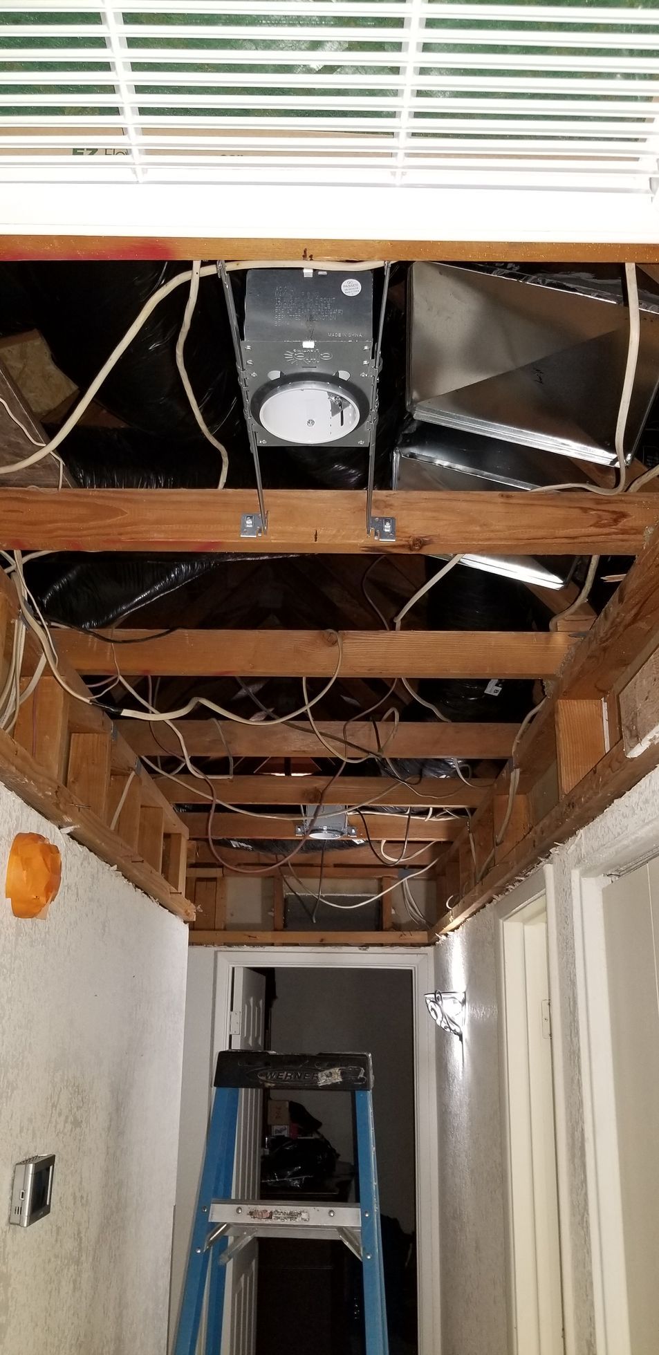 Hallway ceiling with exposed beams and wiring, broken drywall, and a blue ladder below.