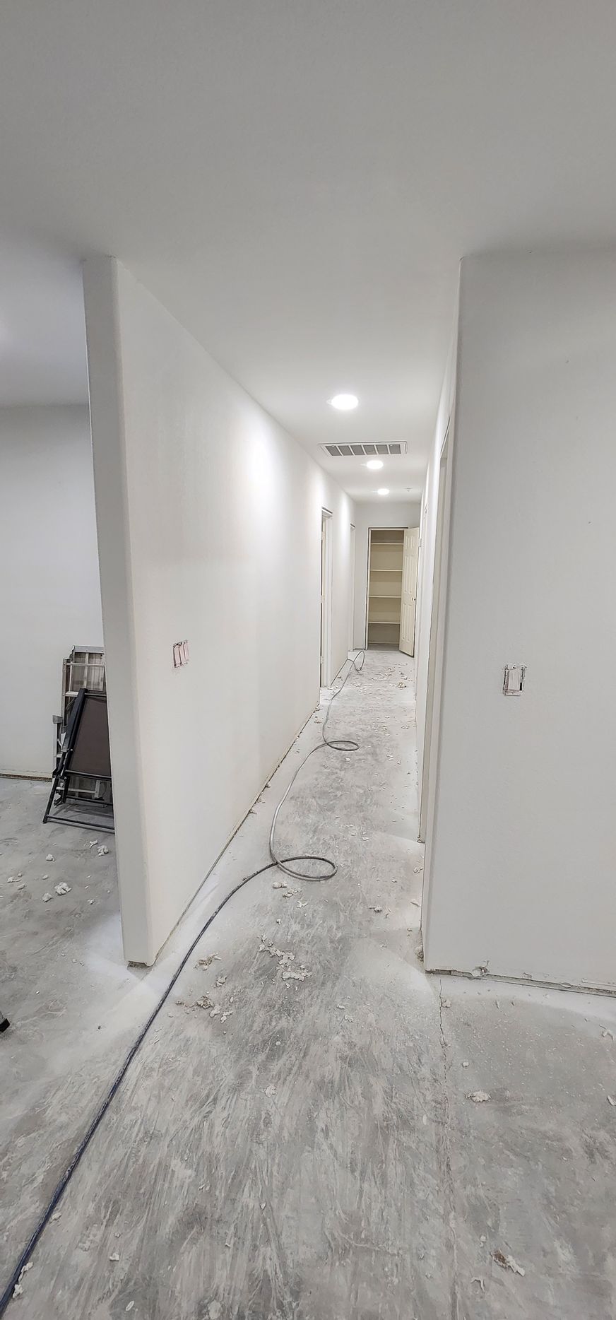 Narrow unfinished hallway with white walls, exposed floors, and construction debris leading to a doorway.