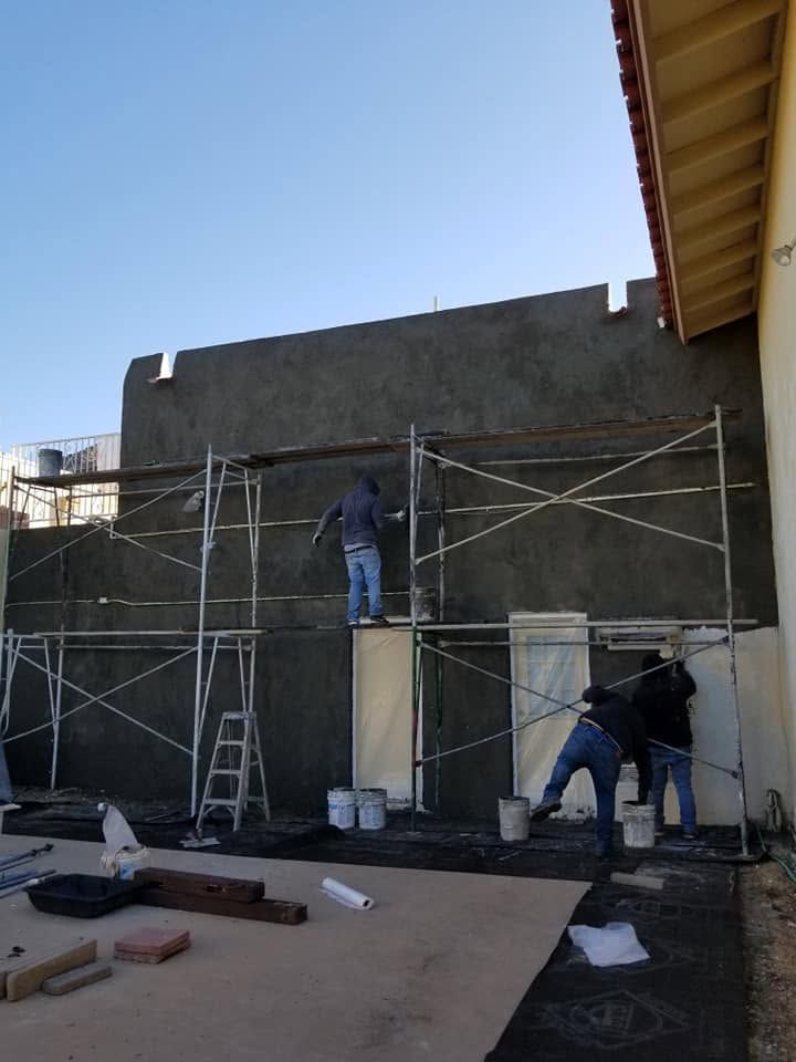Workers on scaffolding plastering a gray exterior wall at a construction site