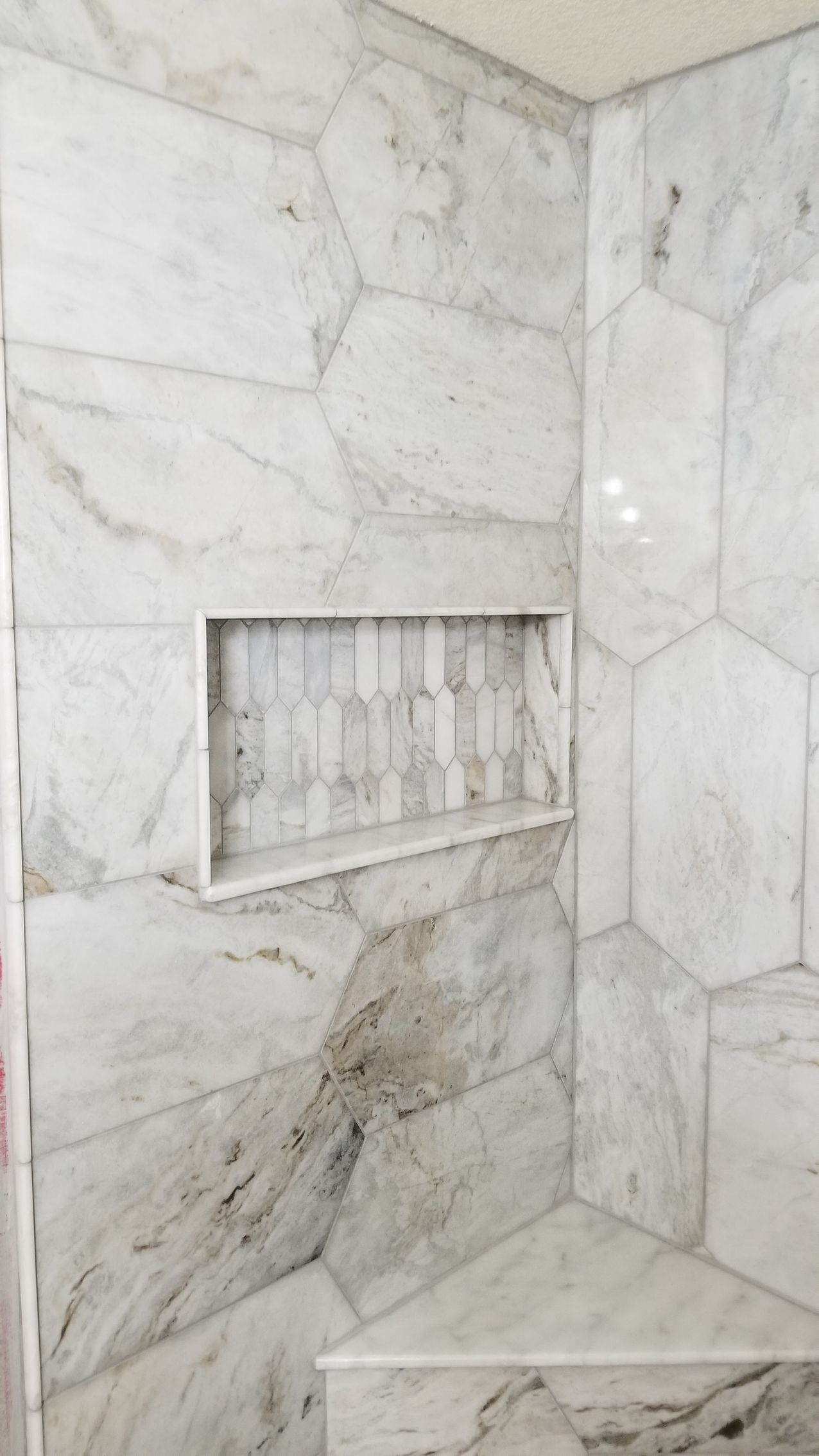 Marble-tiled shower corner with a recessed niche and built-in bench near the bottom.