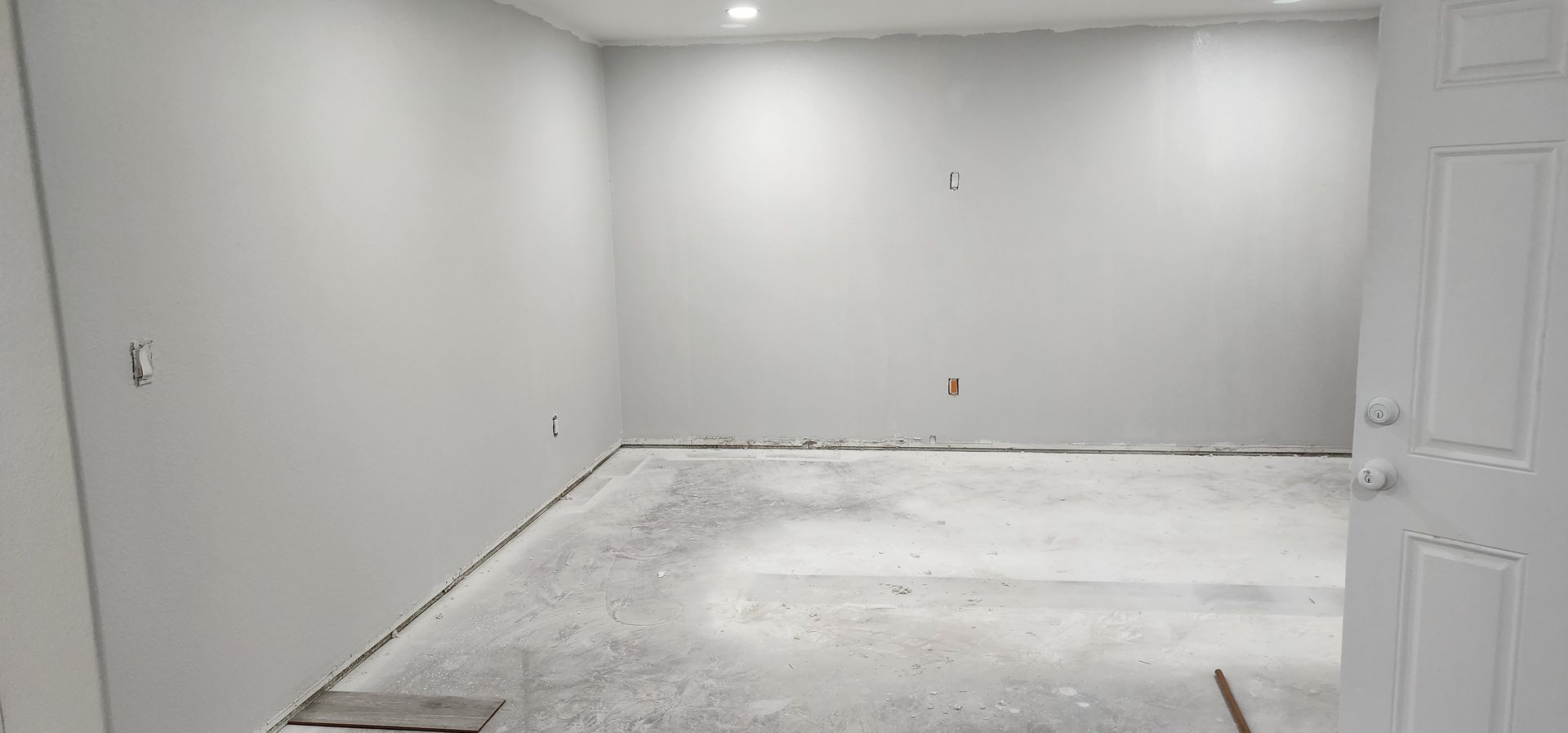 Empty white room under construction with unfinished floor and open door on the right