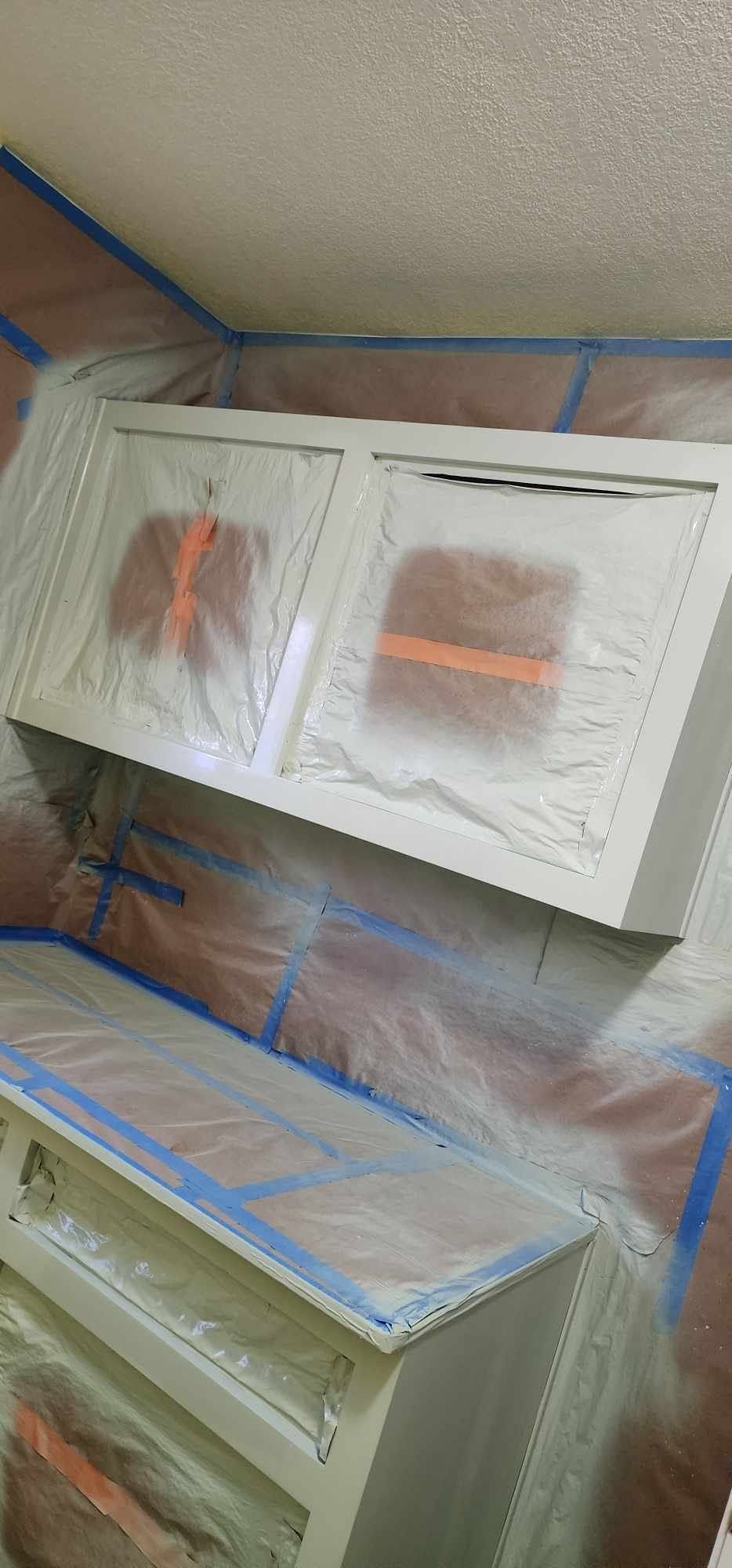 Cabinets and wall paneling masked with plastic and blue painter’s tape during painting prep