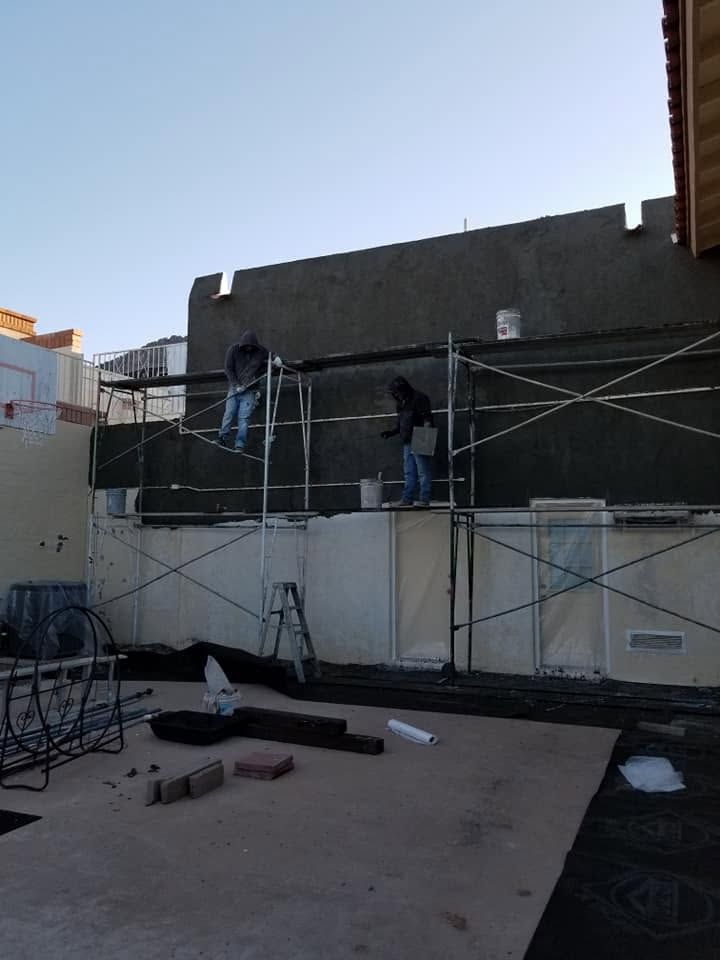 Workers on scaffolding painting a dark wall above a white rooftop patio.