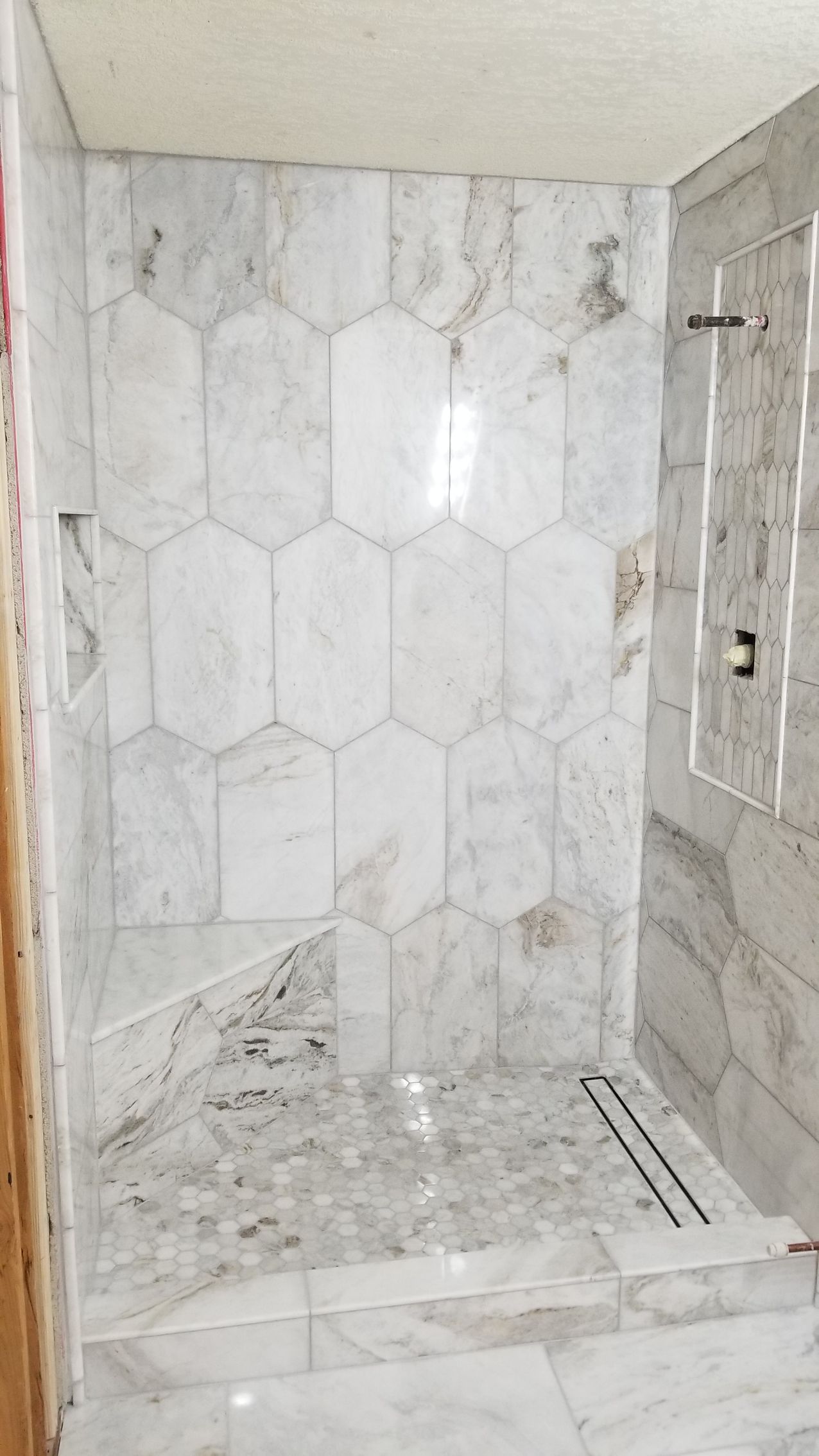 Modern bathroom with white marble tile shower walls and hexagonal floor tile, partially unfinished.