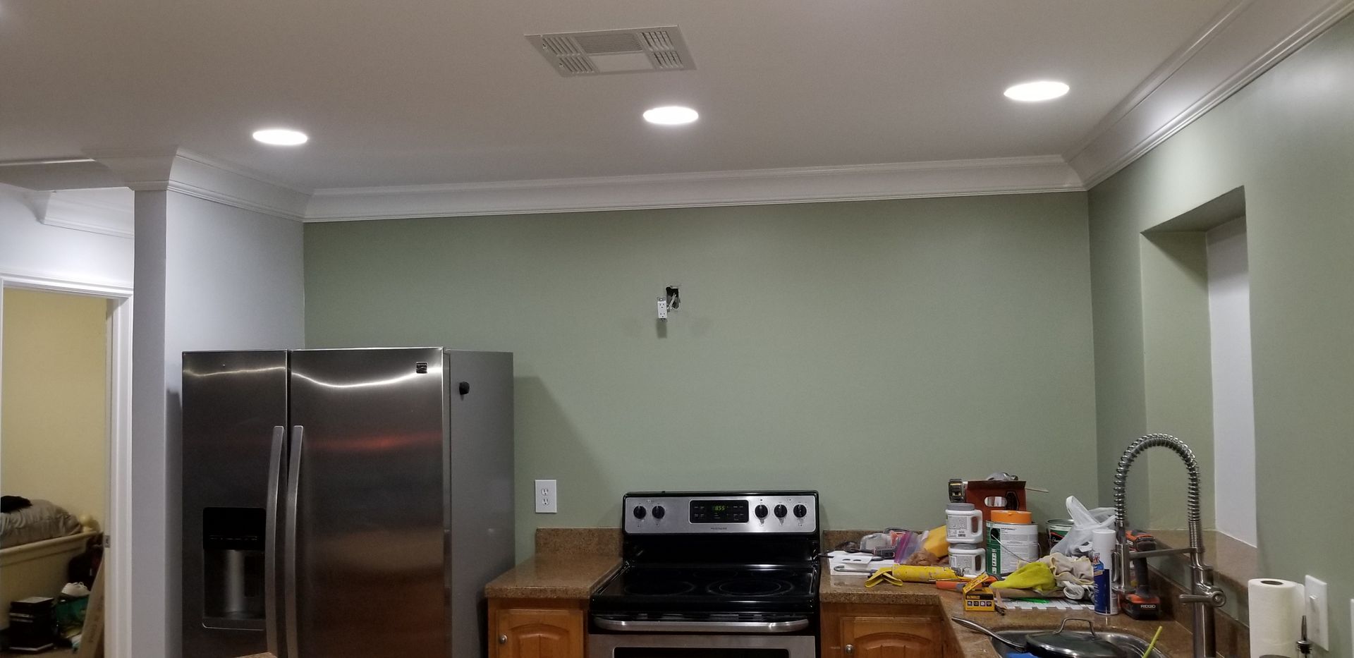 A kitchen with a stainless steel fridge, stove, and countertop cluttered with items under ceiling lights.