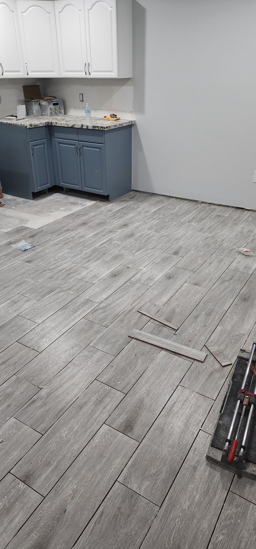 Empty room with gray wood-look flooring and a small blue kitchenette along the left wall