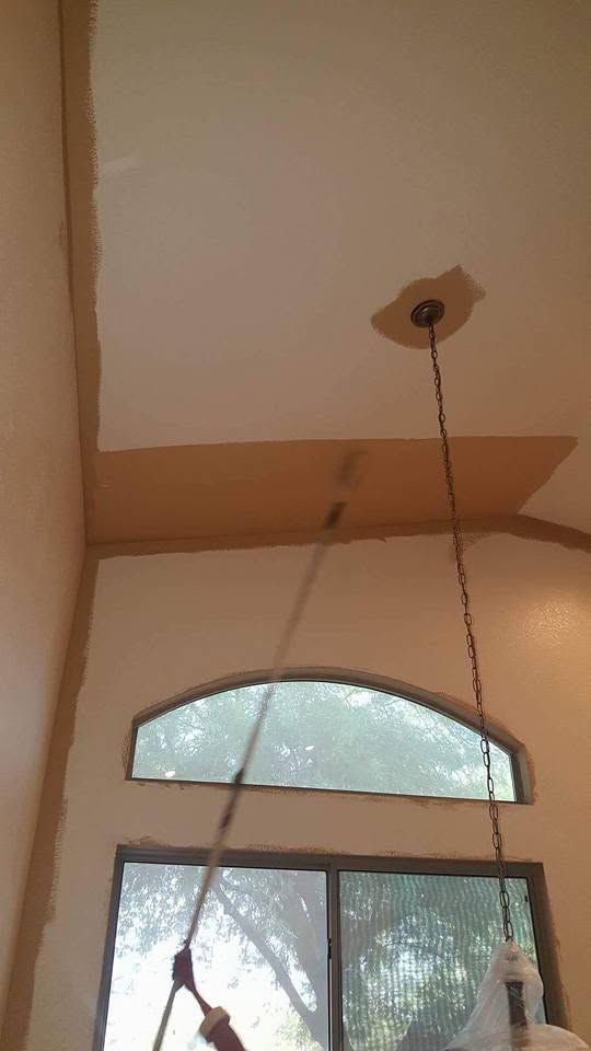 High ceiling with beige walls, arched window, and a hanging pull cord or light fixture.