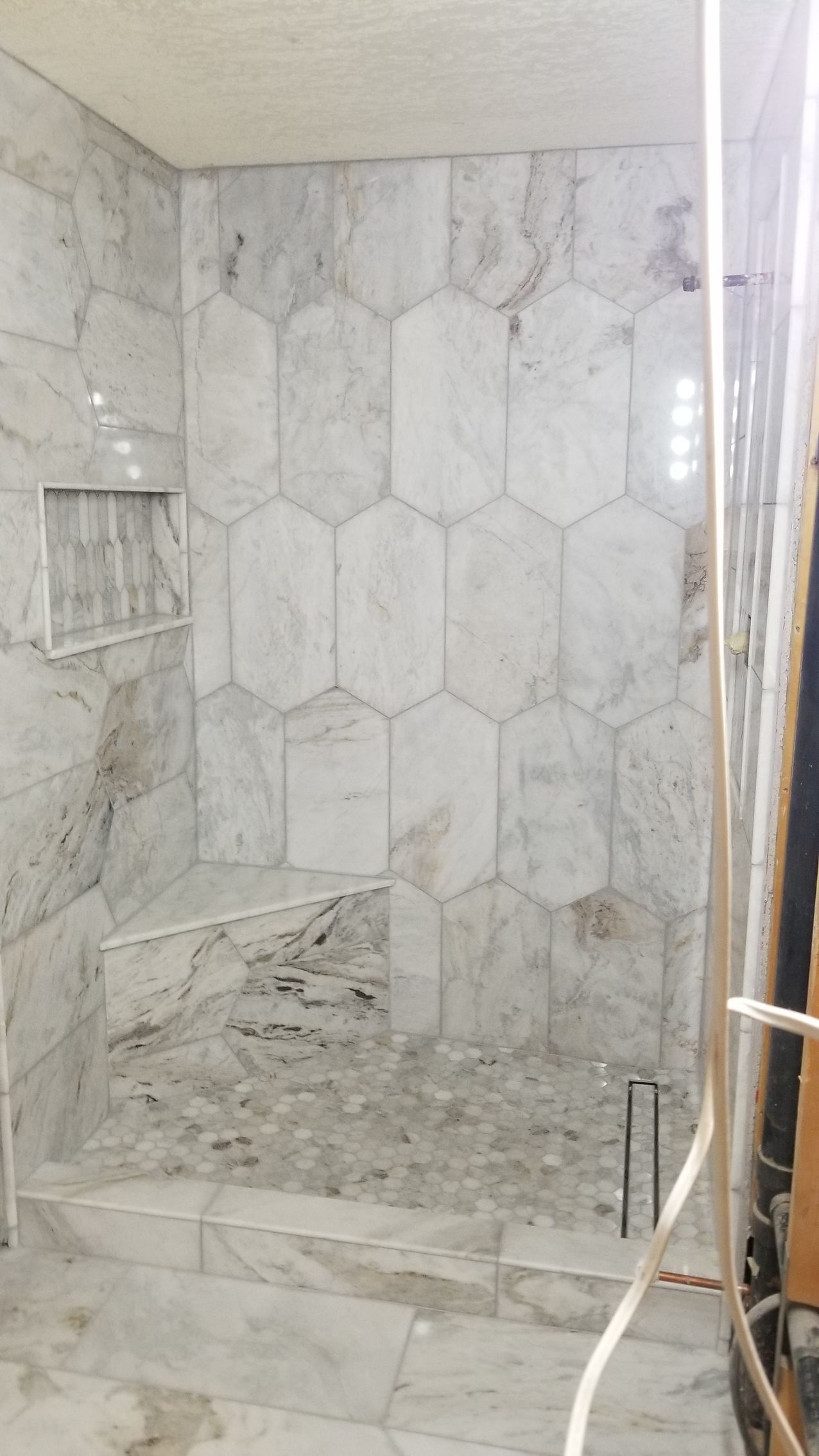 Empty marble-tiled shower stall with a bench and handheld showerhead.