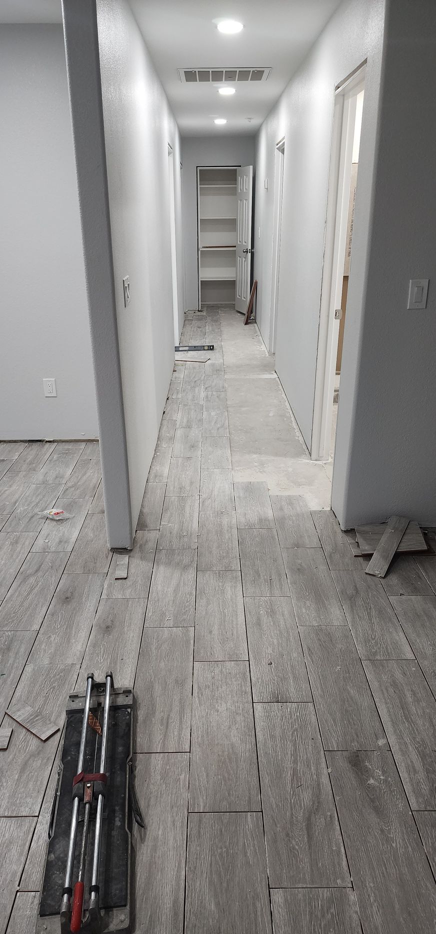 Long hallway with gray tile floor, white walls, and a ladder at the far end.