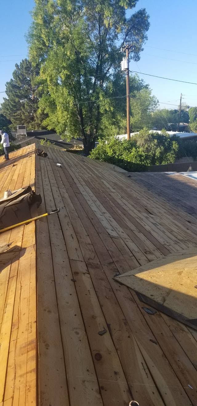 Wooden rooftop deck with railings, trees, and a utility pole in bright daylight