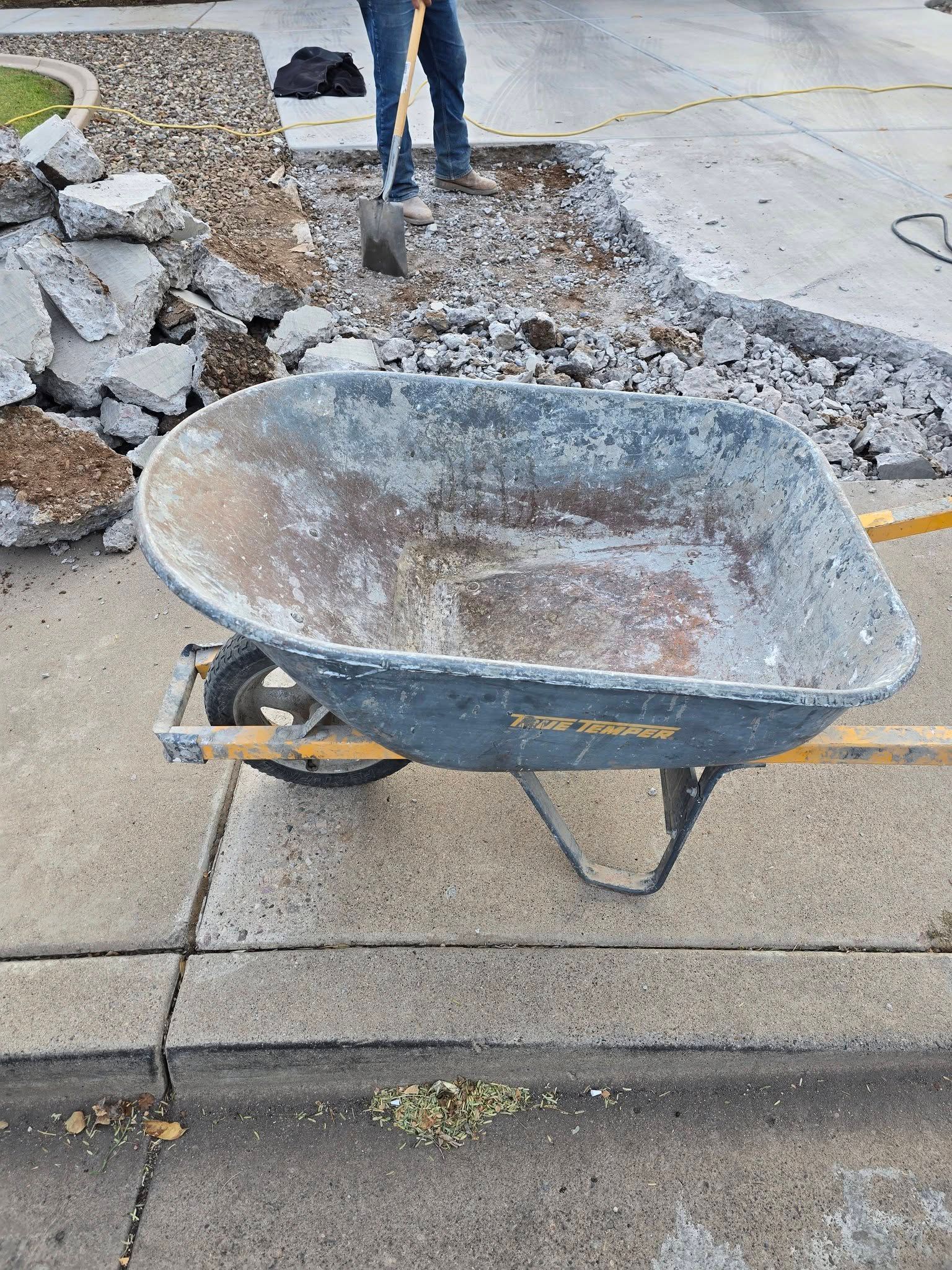 Old, rusty wheelbarrow on a sidewalk beside broken concrete and rubble during repairs