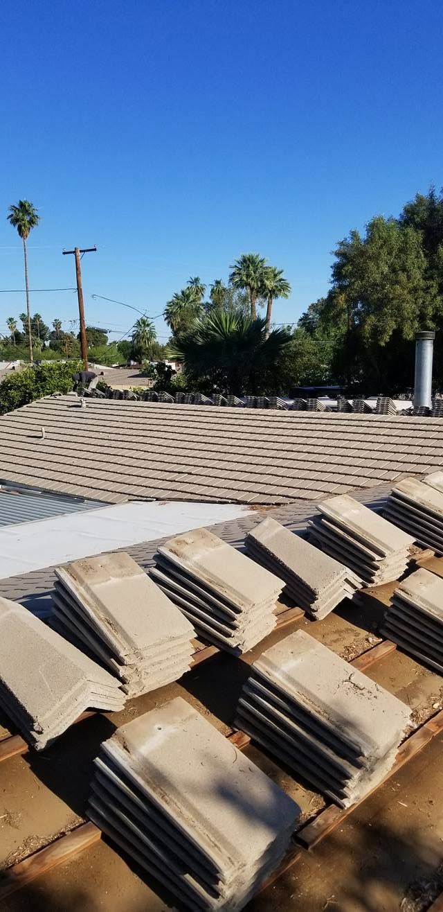 Stacked beige roof tiles in the foreground with palm trees and a clear blue sky behind them.