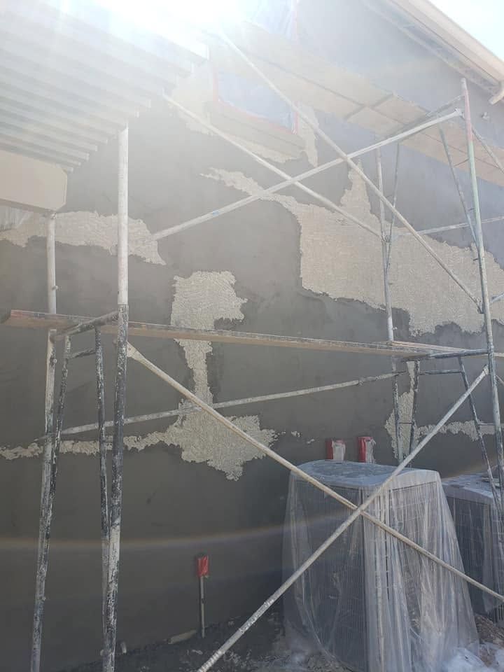 Scaffolding around a partially plastered building wall in bright sunlight