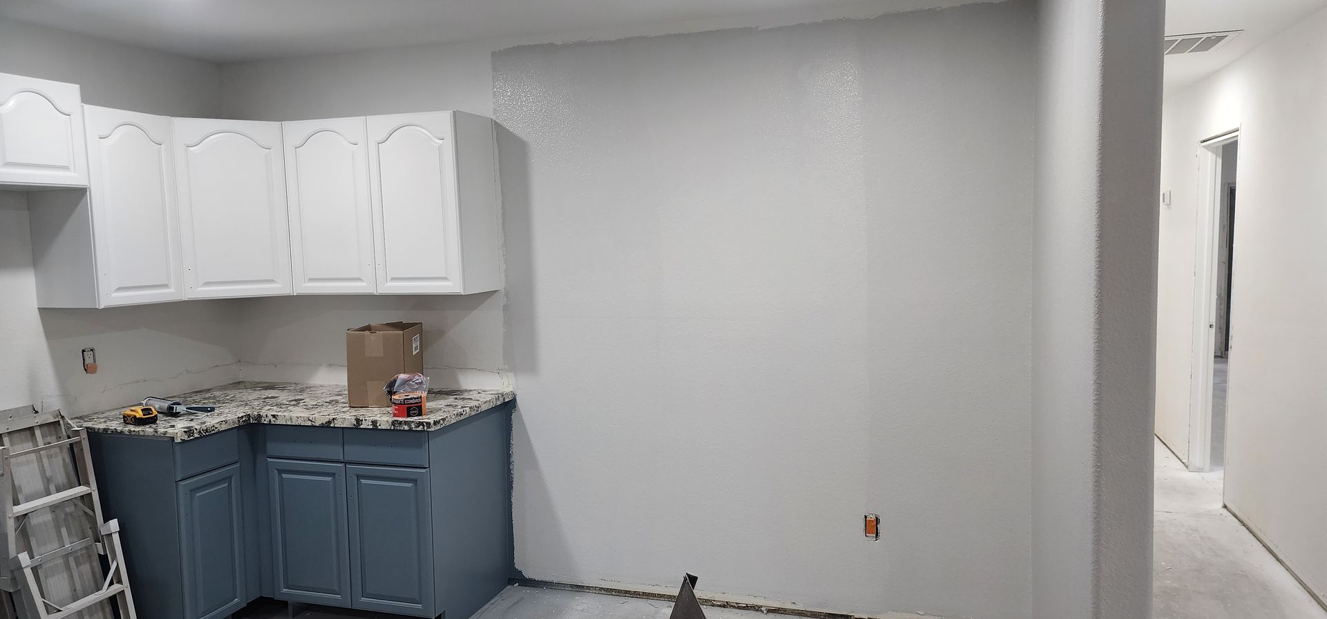Partially renovated kitchen with white cabinets, blue lower cabinets, and bare gray wall