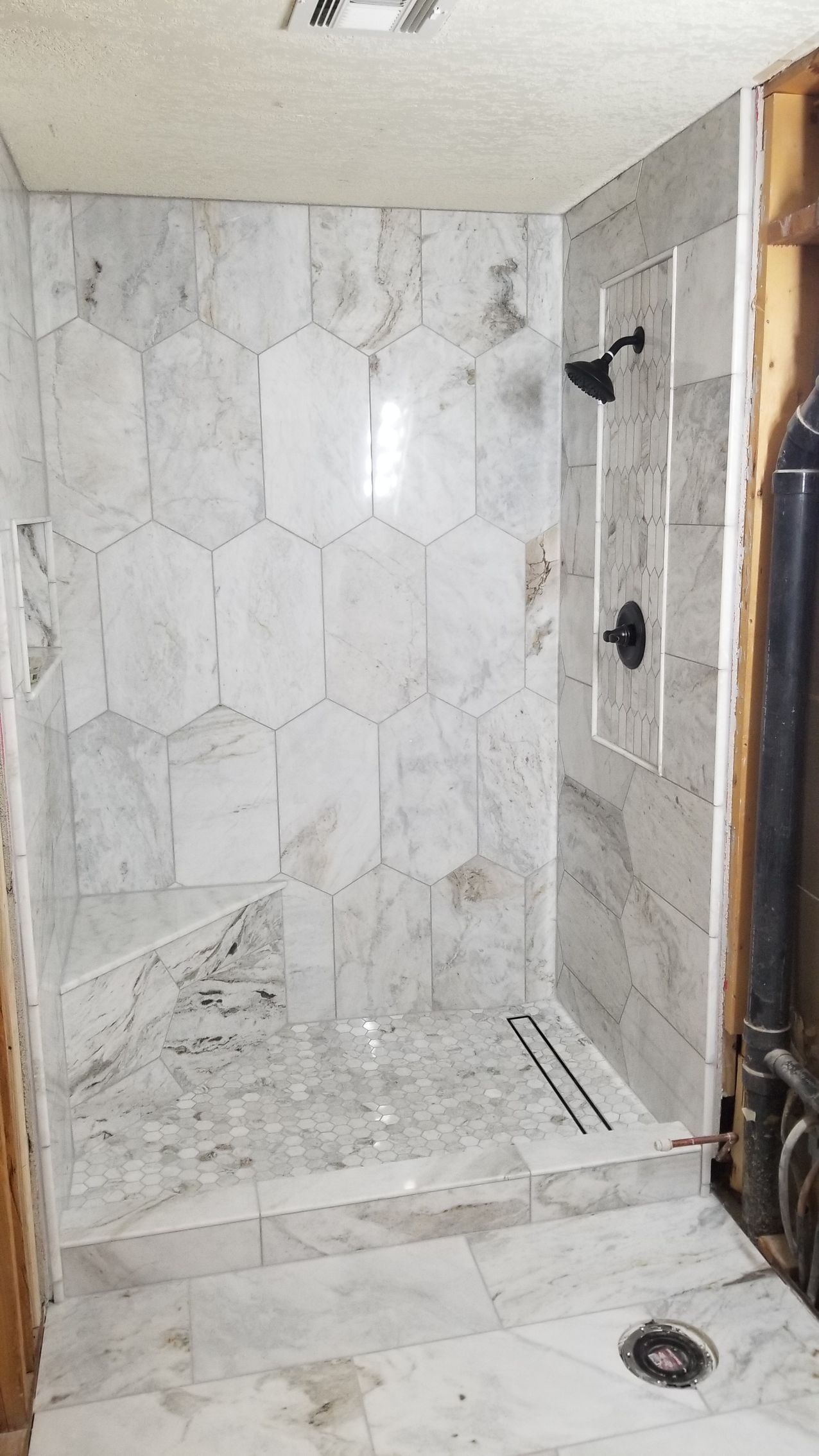 Marble-tiled shower with white walls, built-in bench, and a floor drain