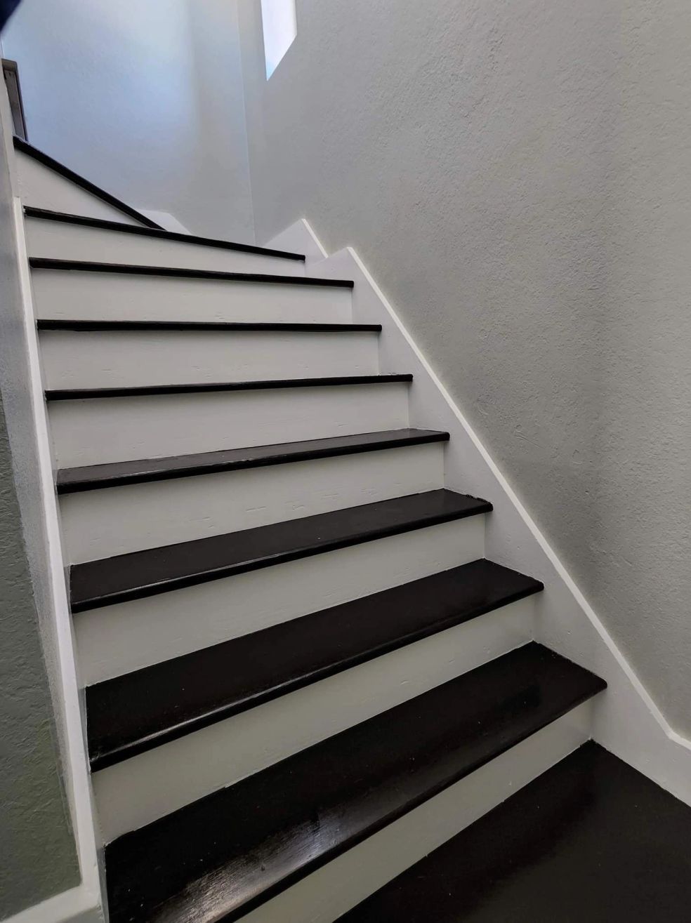 Narrow indoor staircase with white walls and dark-edged steps ascending left to right