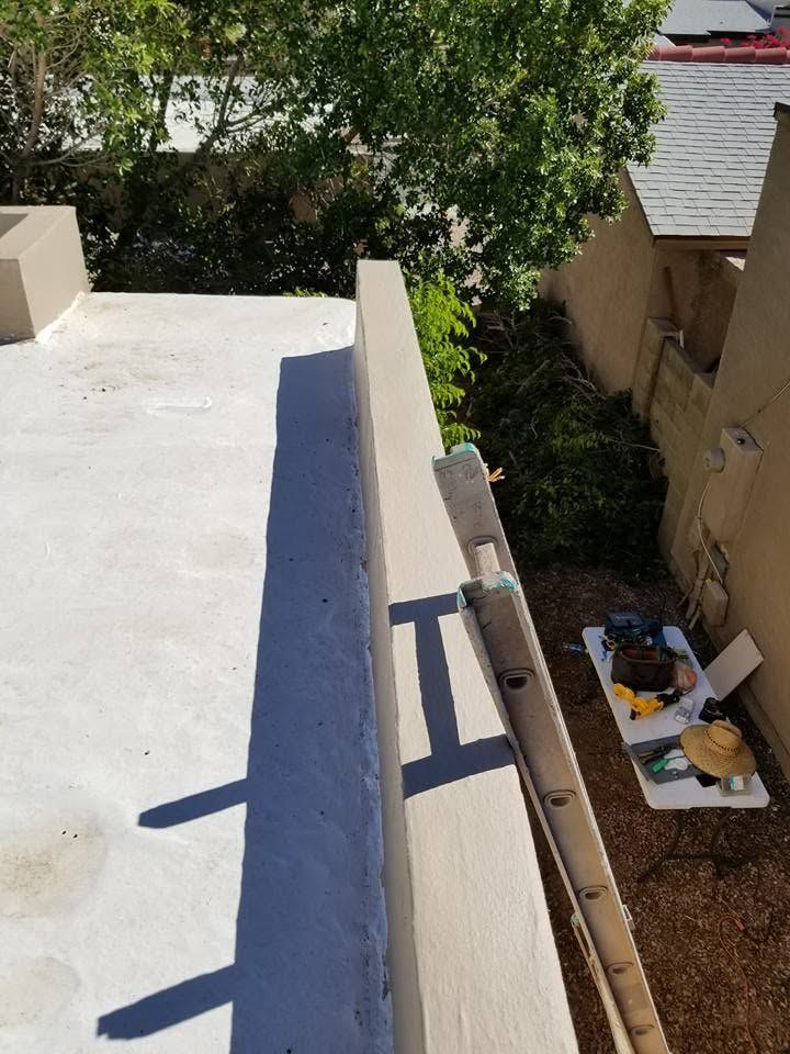 Rooftop view over a narrow alley with trees, tan buildings, and a ladder leaning by the ledge.
