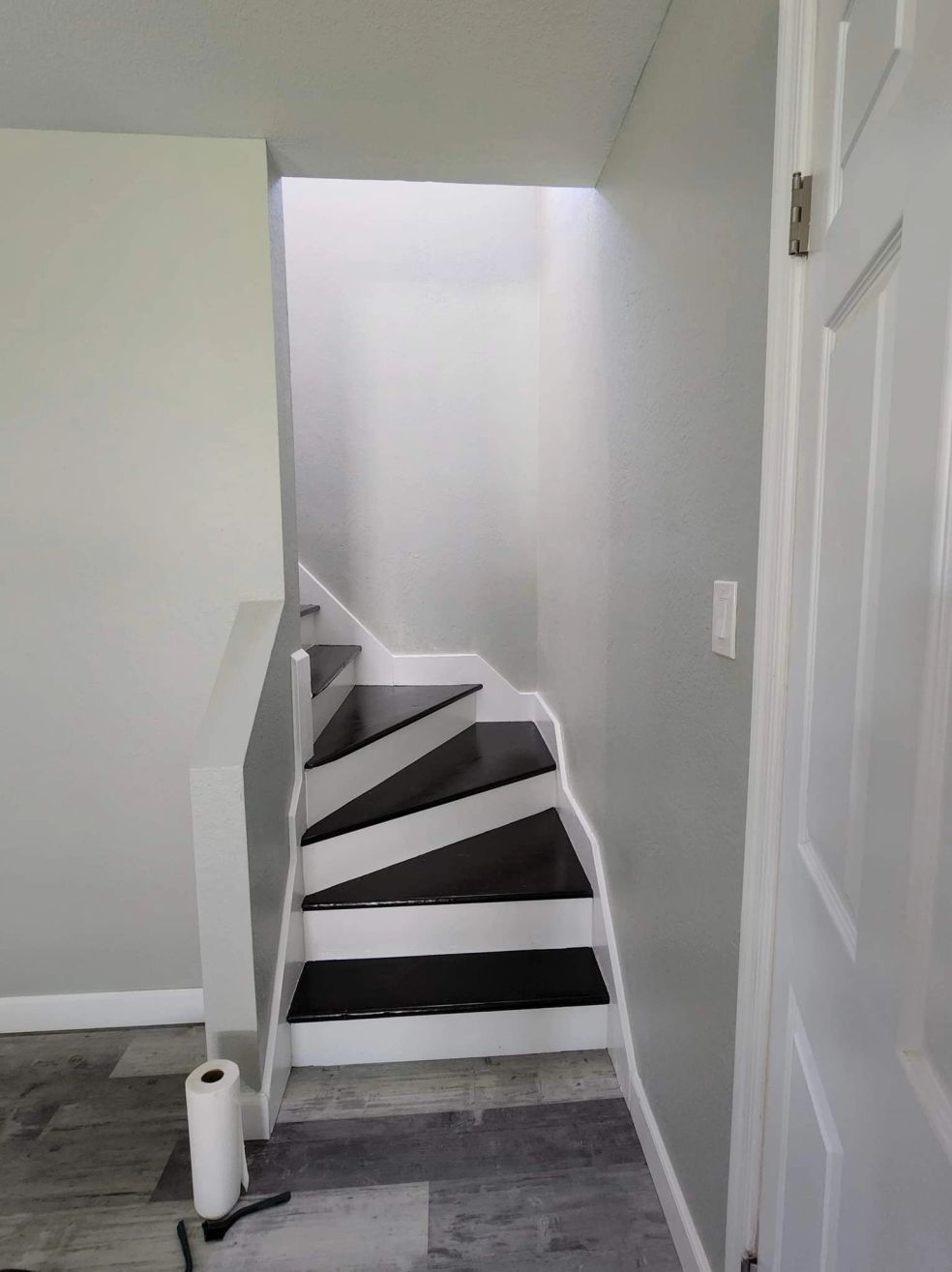 Narrow indoor staircase with dark steps and white railings leading to a bright upstairs landing