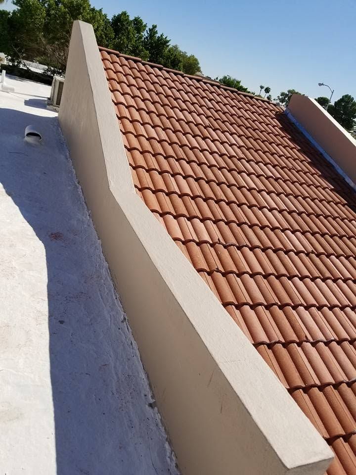 Curved white rooftop wall beside terracotta roof tiles under a clear sky