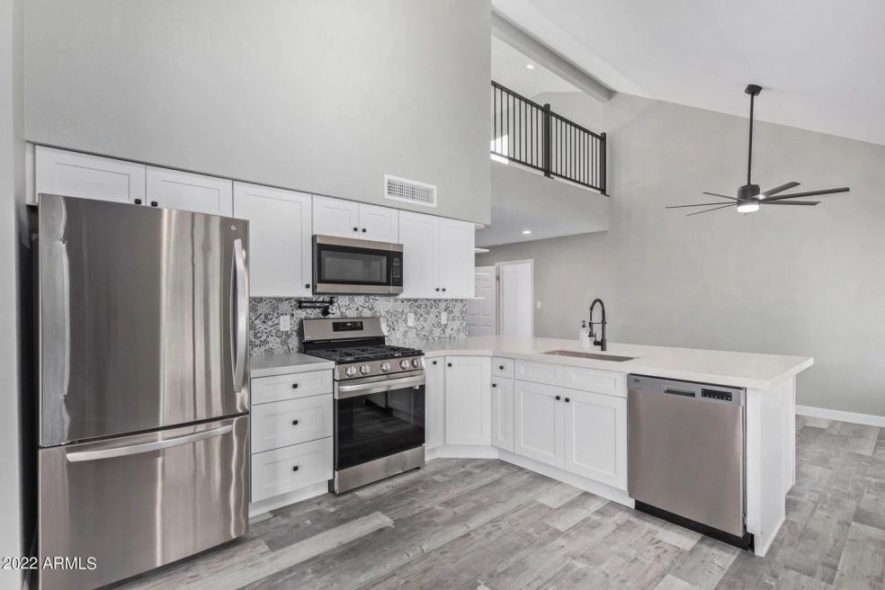 Modern kitchen with stainless steel appliances, white cabinets, island, and ceiling fan in an open layout